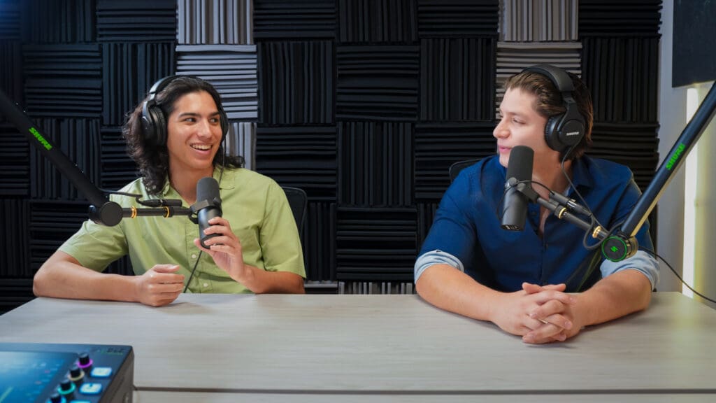 Two male podcast guests speaking to one another with microphones